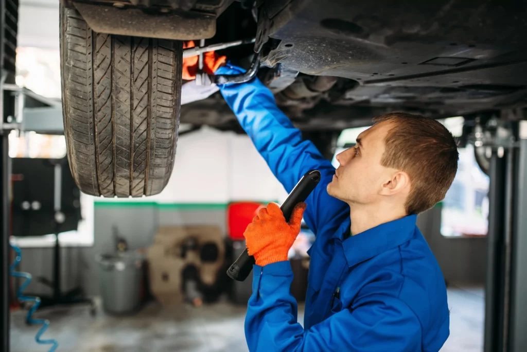 Monteur controleert met een lamp de ophanging van een auto